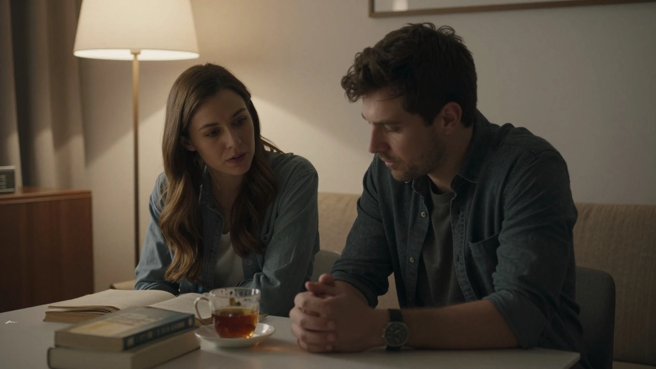 A woman listens empathetically to a man in a softly lit room, books and tea on the table between them.